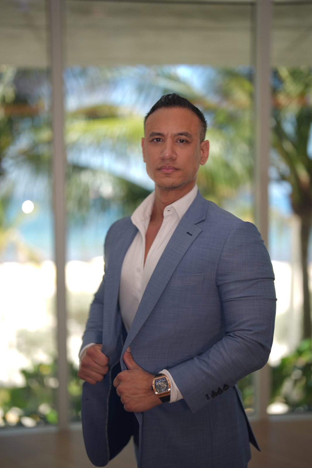 Jibrael Hindi, A Fit Lawyer, in a light-blue suit against a beachfront backdrop